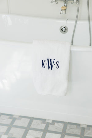 A white towel with a classic navy monogram hangs over the side of a bathtub