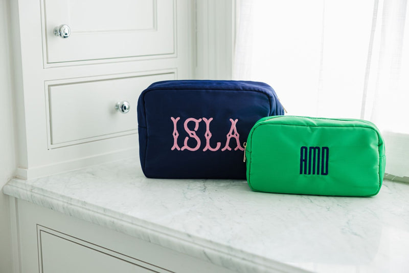 A navy nylon pouch is customized with a pink embroidered name and a green nylon pouch is embroidered with a navy monogram.