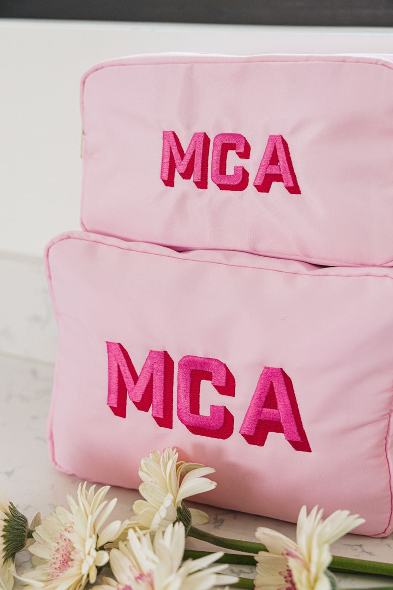 A set of large and extra large nylon pouches are placed atop one another to show the difference in size and show off their pink and red monogram