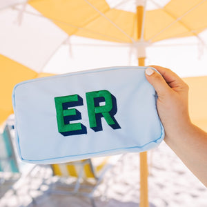 A woman holds a blue pouch with "ER" monogrammed in green
