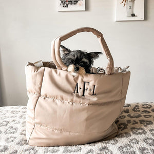 A Yorkie sits in a cream colored puffer tote with a custom monogram