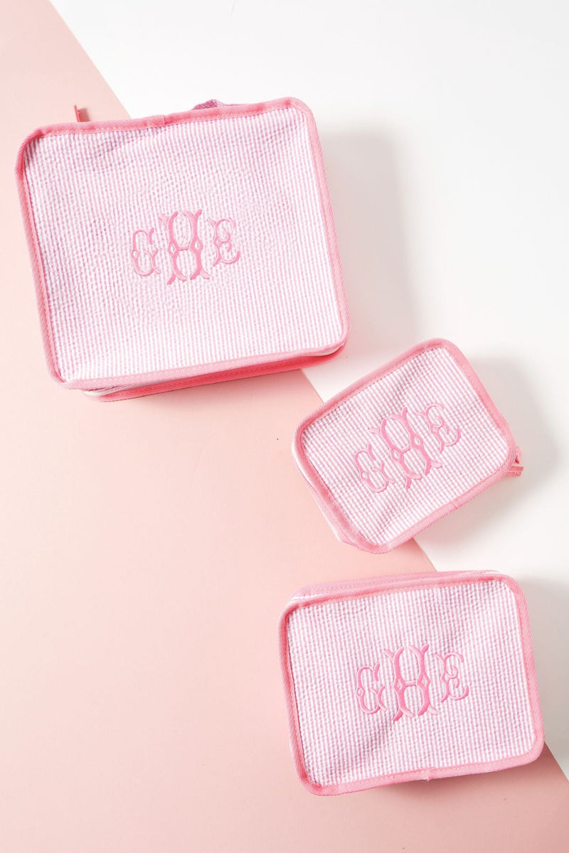 A set of three pink packing cubes is set up to show off their different sizes and embroidered customization.