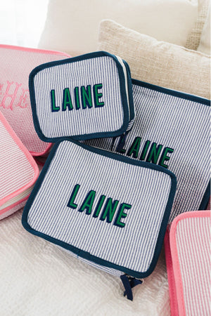 A set of navy packing cubes is customized with a last name in green and navy block font.
