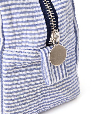 A silver zipper on seersucker pouch is closed showing off the hardware on the pouch