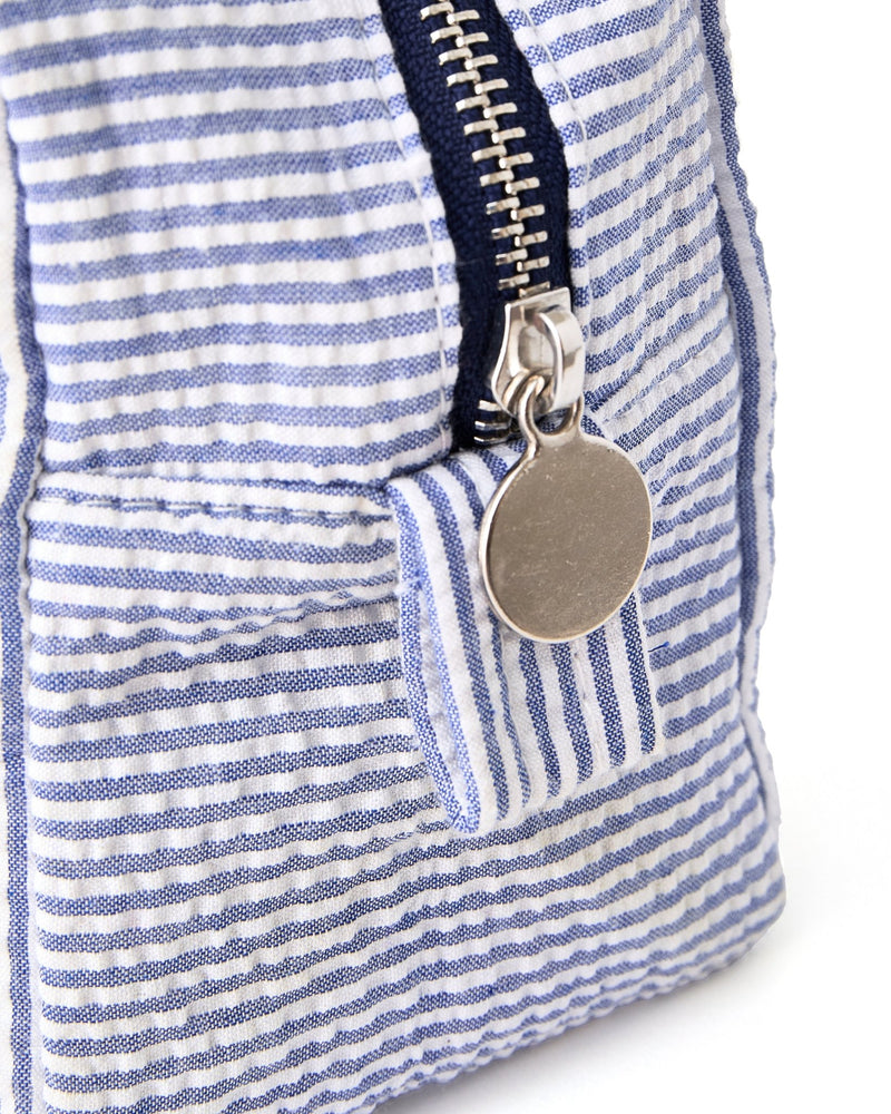 A silver zipper on seersucker pouch is closed showing off the hardware on the pouch