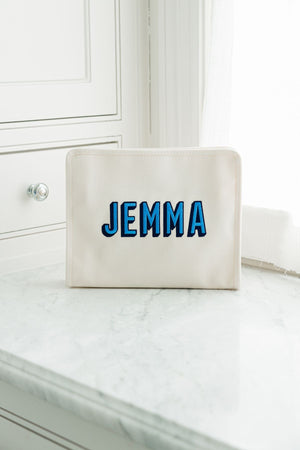 A cream colored roadie is placed on the bathroom counter and personalized with a blue embroidered name.