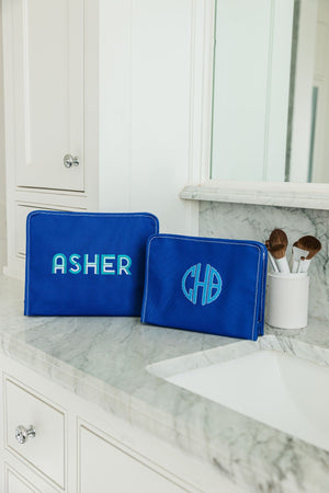Two blue roadies are customized with blue embroidery and placed on a bathroom counter with some makeup brushes.