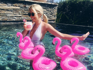 A woman sits in the pool with her custom flamingo drink floats and custom wine glass.