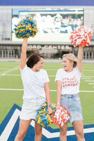 Two women standing on a football field wear custom gameday tees that match their pompoms.