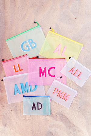 A large collection of our pool bag colors and sizes sits in the sand