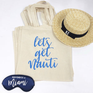 A stack of totes that say "let's get nauti" is paired with a custom boater hat and navy sleep mask.