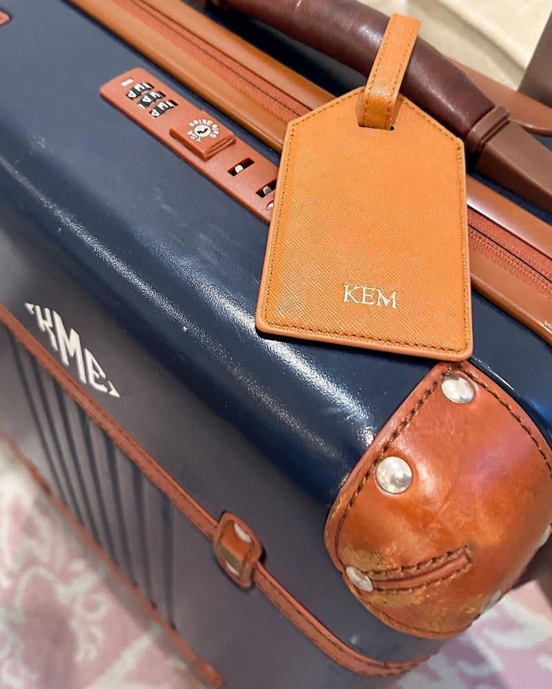 A tan luggage tag has a monogram with gold foiling for the letters
