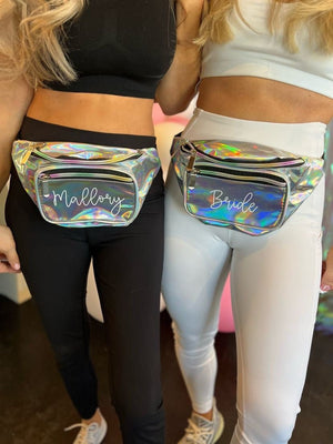 Two girls wear silver metallic fanny packs with white script names printed on them