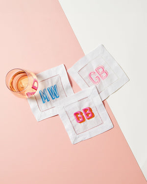 A wine glass sits on three embroidered cocktail napkins which are customized with different monograms and thread colors.