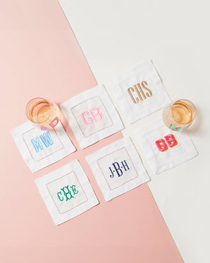 Six monogram cocktail napkins are set out with wine glasses to show off some of the embroidered monograms that can customize your cocktail napkins.