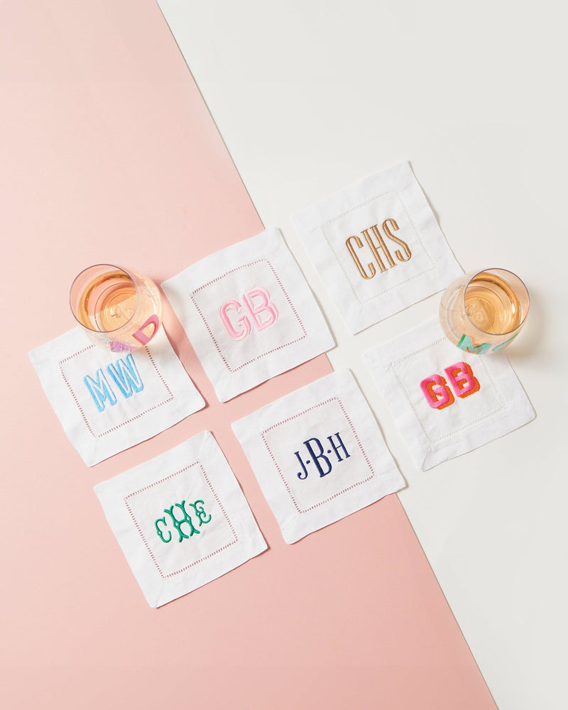 Six monogram cocktail napkins are set out with wine glasses to show off some of the embroidered monograms that can customize your cocktail napkins.