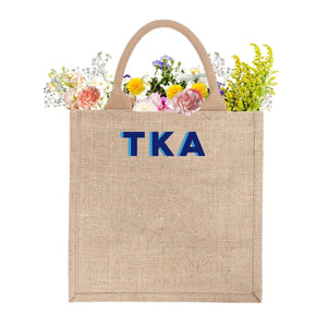 A custom jute bag has "TKA" monogrammed on the front in blue