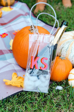 A clear bag is customized with a pink and orange monogram and filled with ice and a bottle of alcohol.