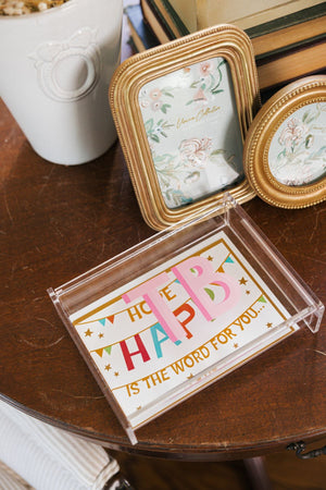 A pink monogrammed acrylic catchall box is used to collect cards on a brown wooden table.