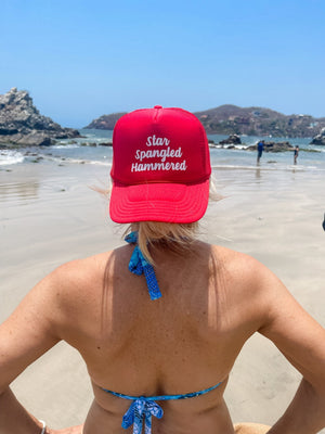 A woman on the beach wears a hat that says "Star Spangled Hammered"