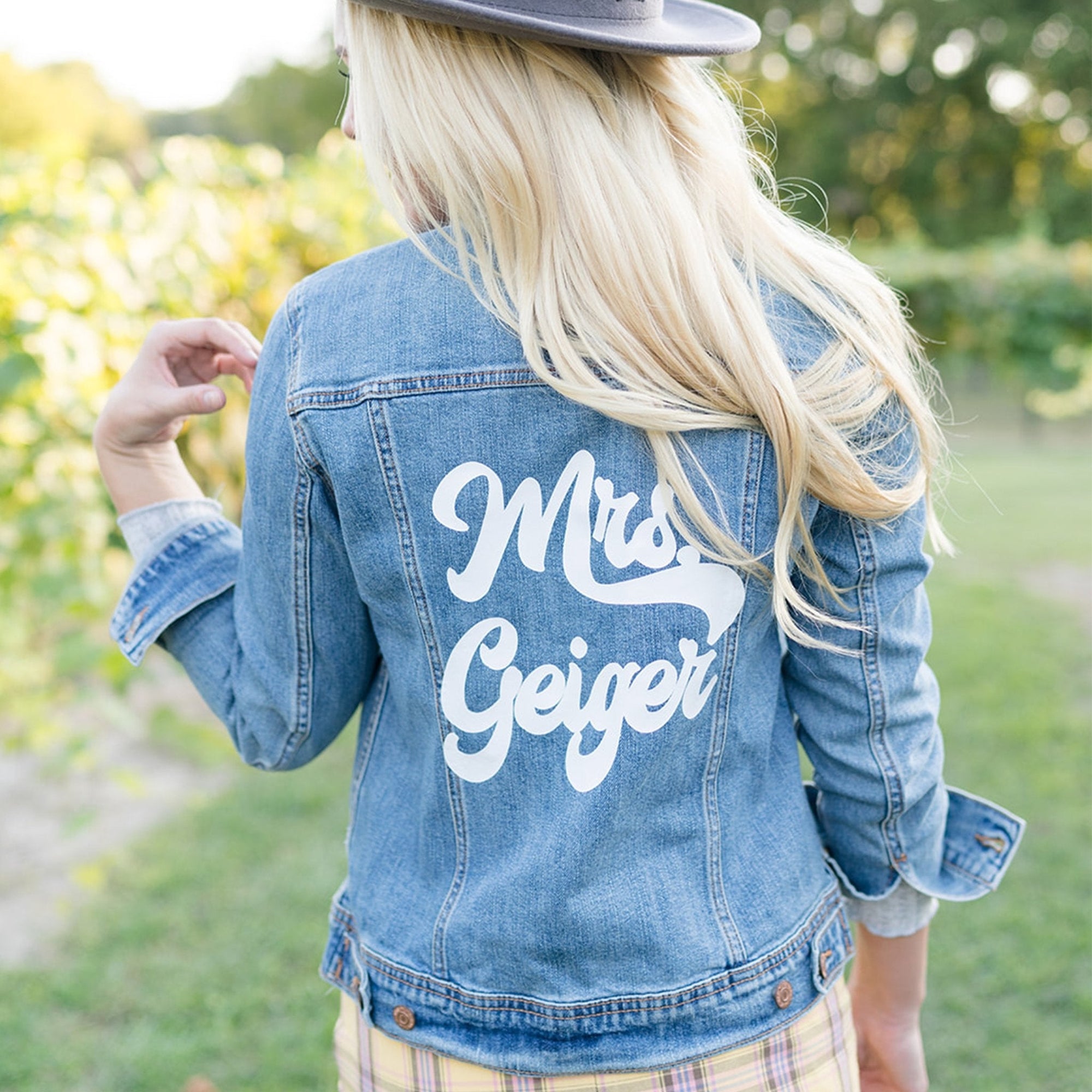 A woman shows off her custom retro denim jacket which reads "Mrs. Goswick" in white text across her shoulders.