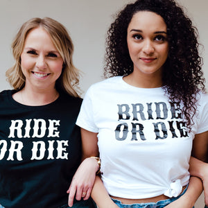 Two girls stand together wearing black and white "Bride or Die" shirts.