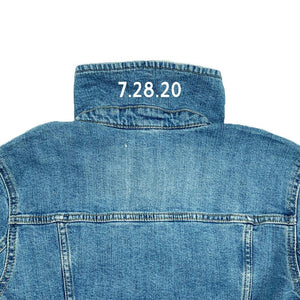 A jean jacket is customized with a date in white text on the collar.