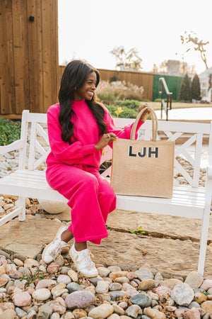A woman in a pink outfit sits on a park bench with her customized jute tote.
