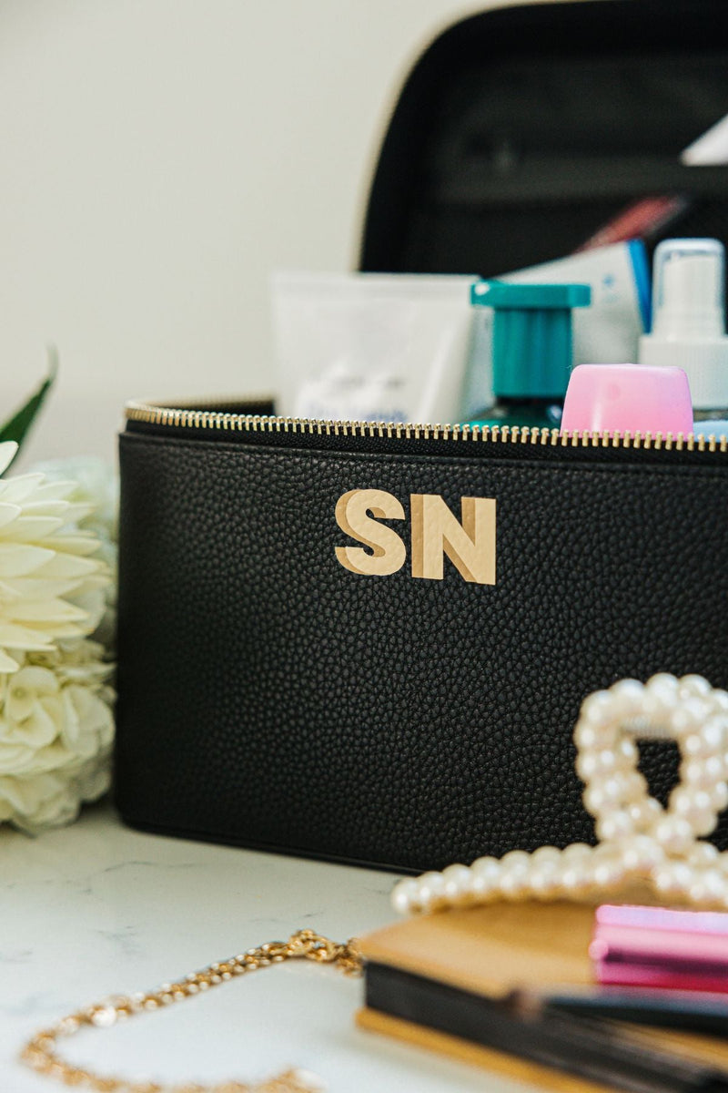 A black train case is personalized with a neutral colored monogram on the front.