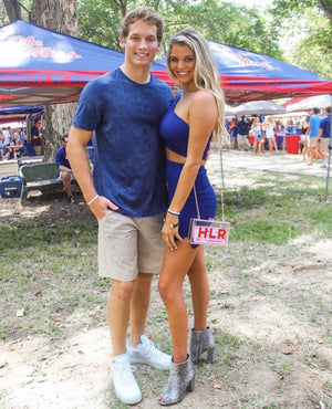 A woman shows off her stadium bag customized with her initials in red at a tailgate.
