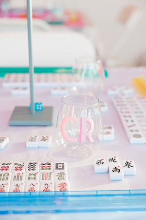 A wine glass with pink C and R initials in a shadow monogram font on it, next to mahjong tiles 