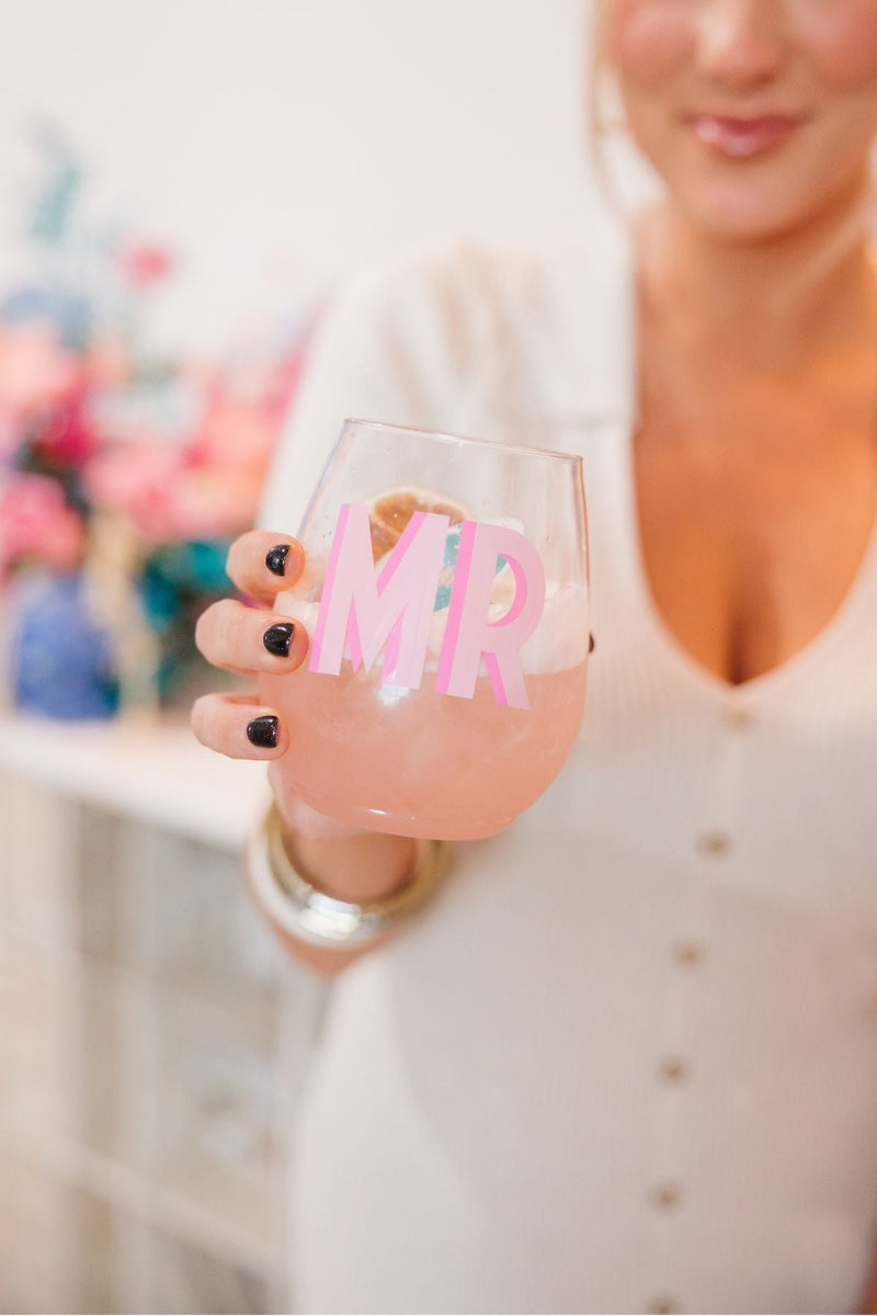 A person holding a stemless wine glass with pink shadowed initials on it