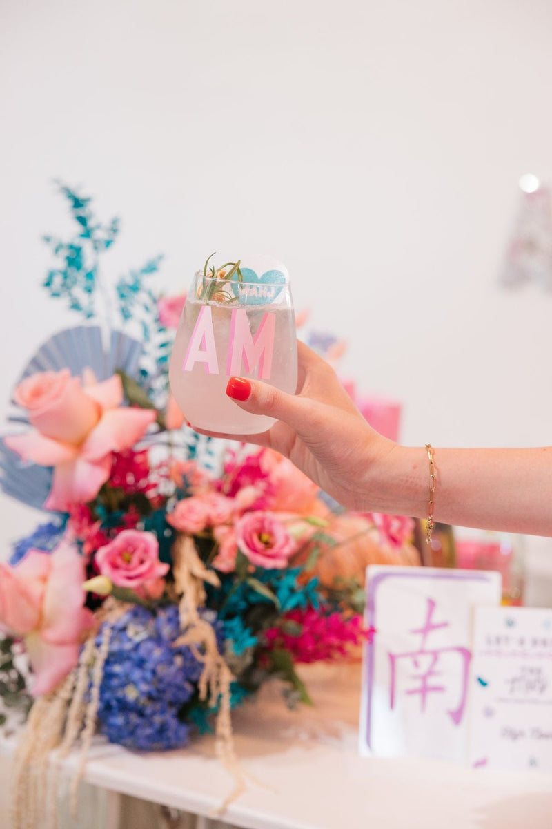 A woman holding a personalized stemless wine glass that has a pink initials on it at a party 