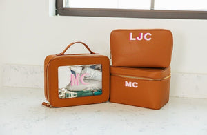 A collection of tan leather travel cases are monogrammed with pink letters.