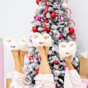 Three people hold up their feet wearing white slippers customized with names