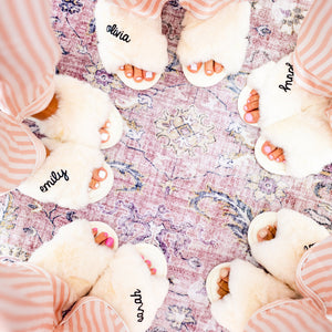 A group of girls in pink striped pajamas wear white slippers with custom names printed on them