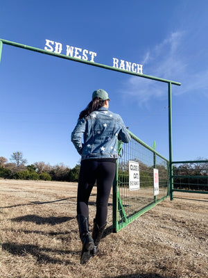 A woman stands at a gate wearing a customized jean jacket with white stars.