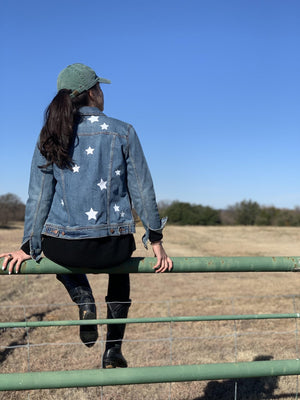 A woman sits in a field wearing a custom jean jacket with white stars.
