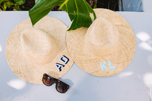 Two monogrammed straw beach hats with blue embroidery