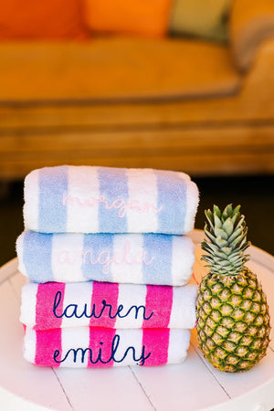 A stack of blue and pink cabana towels are customized with embroidered names.