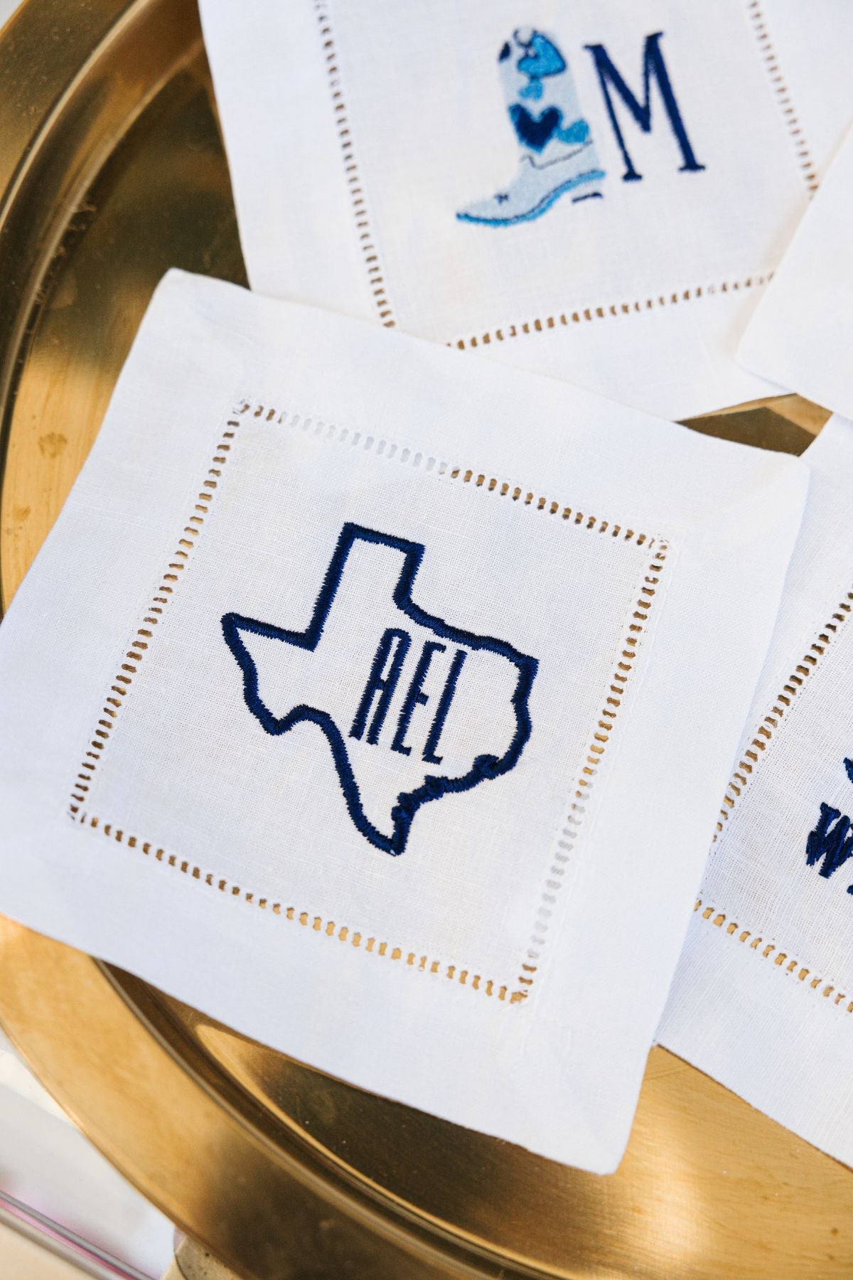 An embroidered cocktail napkin with a monogram and the Texas state outline in navy.