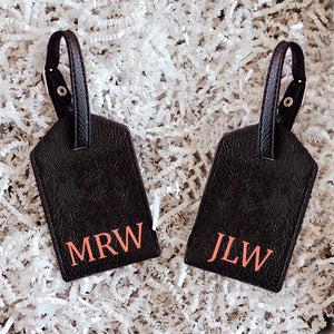 Two black luggage tags are personalized with monograms in a melon font