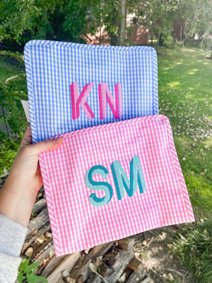 A person holds up a blue and pink gingham pouch with monograms embroidered on them.
