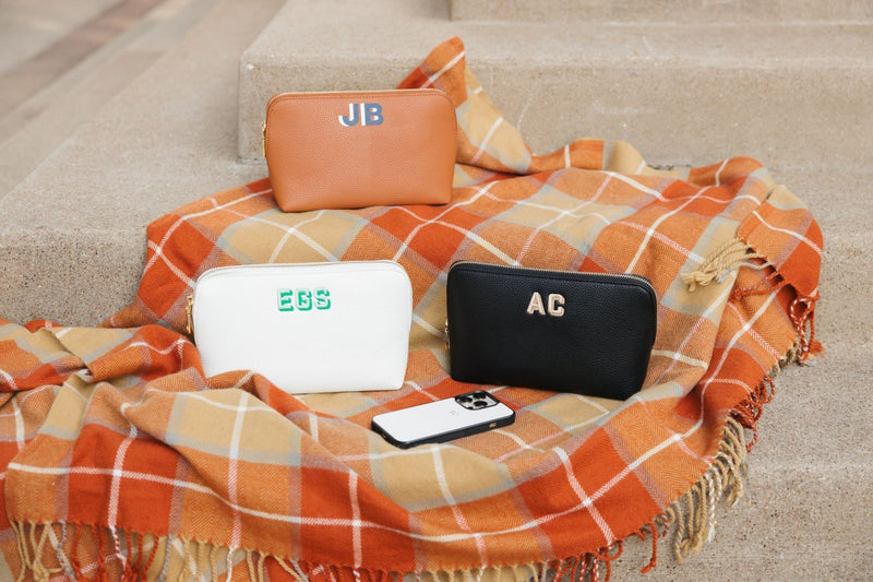 Three vegan leather pouches in white, black, and tan sit on an orange flannel blanket