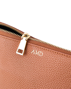 A tan leather pouch is monogrammed with a gold embossing.