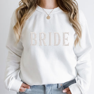 A woman wears a white sweatshirt with "Bride" embroidered on the front