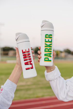 Two white 24 oz flip-top tumblers personalized with red-plaid “LAINE” and green-yellow “PARKER.”