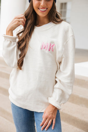 A woman smiles standing in her cream corded sweatshirt with a pink shadow monogram.