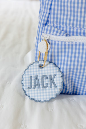 Blue backpack with a gold carabeener and bag tag on the zipper pull that says Jack.