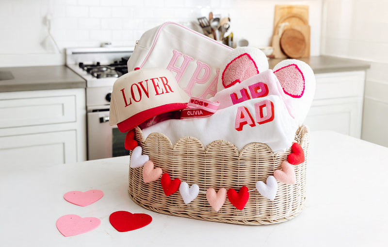 Teen valentine's day basket filled with personalized sprinkled with pink merchandise: lover hat, name bracelets, monogram sweatshirts, fuzzy slippers, and monogrammed canvas pouch